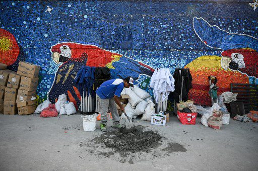 Un trabajador mezcla cemento para usar en un mural hecho con tapas de botellas de plástico por el artista venezolano Oscar Olivares en Guatire, estado de Miranda, Venezuela, el 13 de septiembre de 2022. 