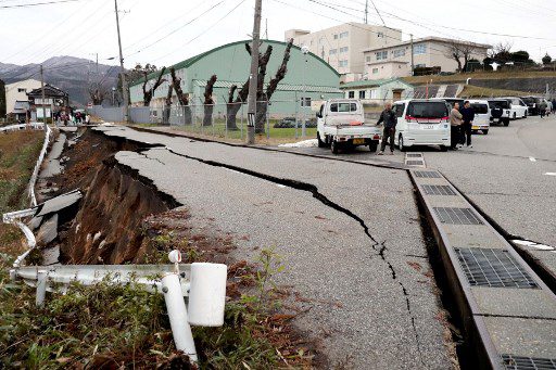 La gente se encuentra junto a grandes grietas en el pavimento después de ser evacuada a una calle en la ciudad de Wajima, prefectura de Ishikawa, el 1 de enero de 2024, después de que un gran terremoto de magnitud 7,5 sacudiera la región de Noto en la prefectura de Ishikawa por la tarde. Olas de tsunami de más de un metro de altura azotaron el centro de Japón el 1 de enero después de una serie de poderosos terremotos que dañaron casas, cerraron carreteras y llevaron a las autoridades a instar a la gente a huir a terrenos más altos